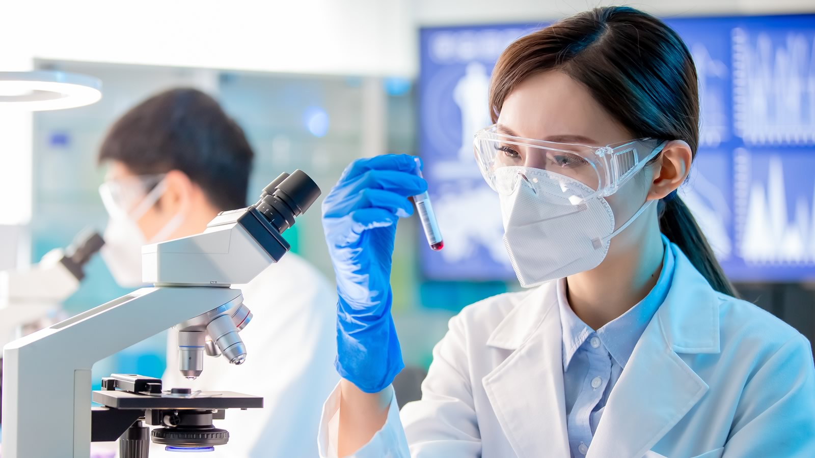 Scientist inspecting a vial in front of a microscope